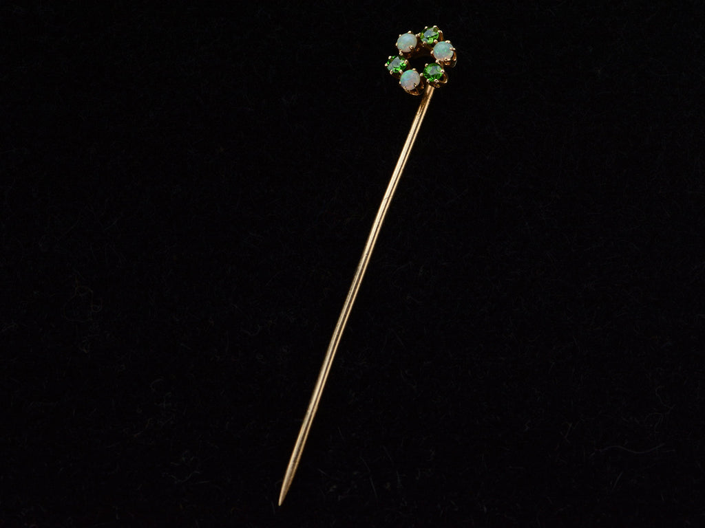 An antique yellow gold Victorian stick pin with three opals and three vivid green demantoid garnets arranged in a circle. Shown on black background.