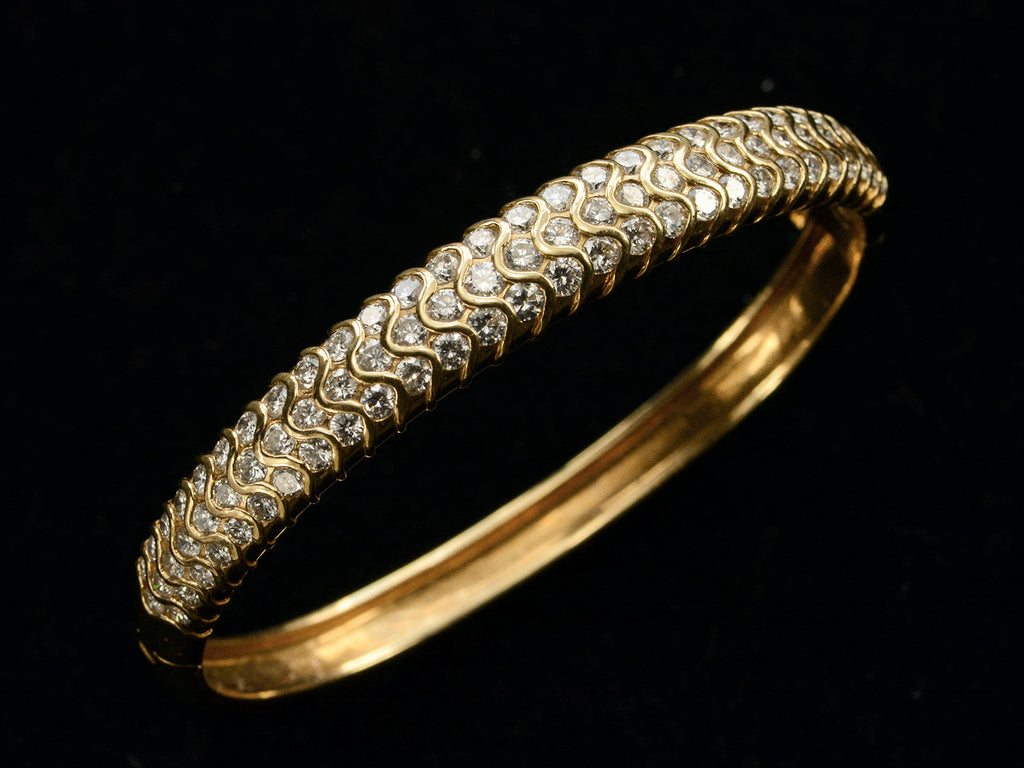 Angled view of a vintage 18K yellow gold bracelet set with three rows of round white diamonds in a fish-scale like pattern, shown on dark background.