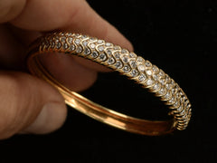 thumbnail of Hand holding a vintage 18K yellow gold bracelet set with three rows of round white diamonds in a fish-scale like pattern, shown on dark background.