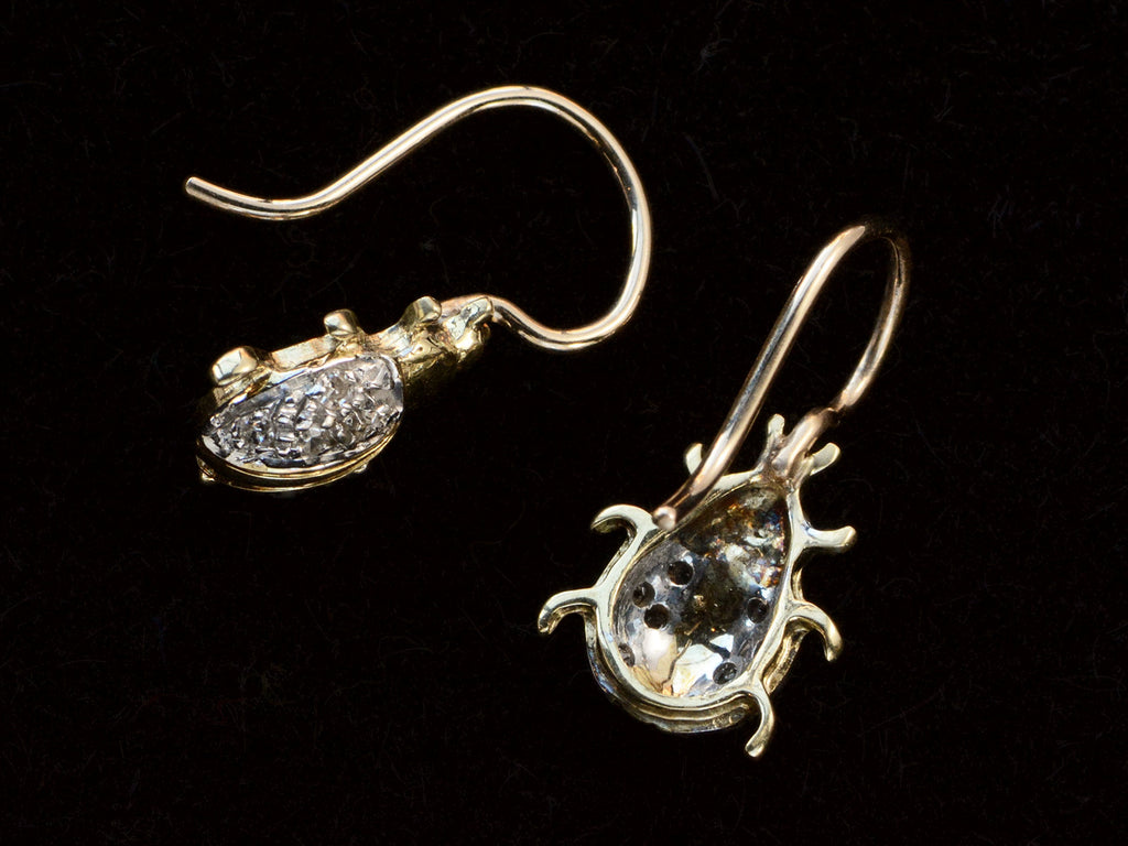 Side and reverse side detail views of a pair of vintage bug-shaped earrings in yellow gold with white gold details and single cut diamonds set in the bodies. On black background.
