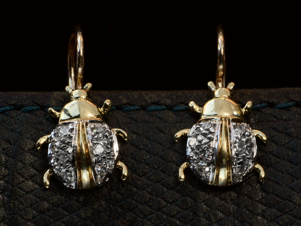 A pair of vintage bug-shaped earrings in yellow gold with white gold details and single cut diamonds set in the bodies. On dark background.