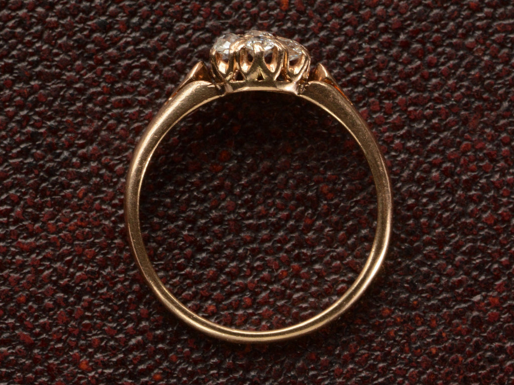 Side profile of an antique rose gold Victorian ring with seven old European cut diamonds set in a cluster. Shown on dark textured background.