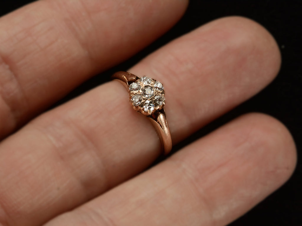 An antique rose gold Victorian ring with seven old European cut diamonds set in a cluster. Shown on finger