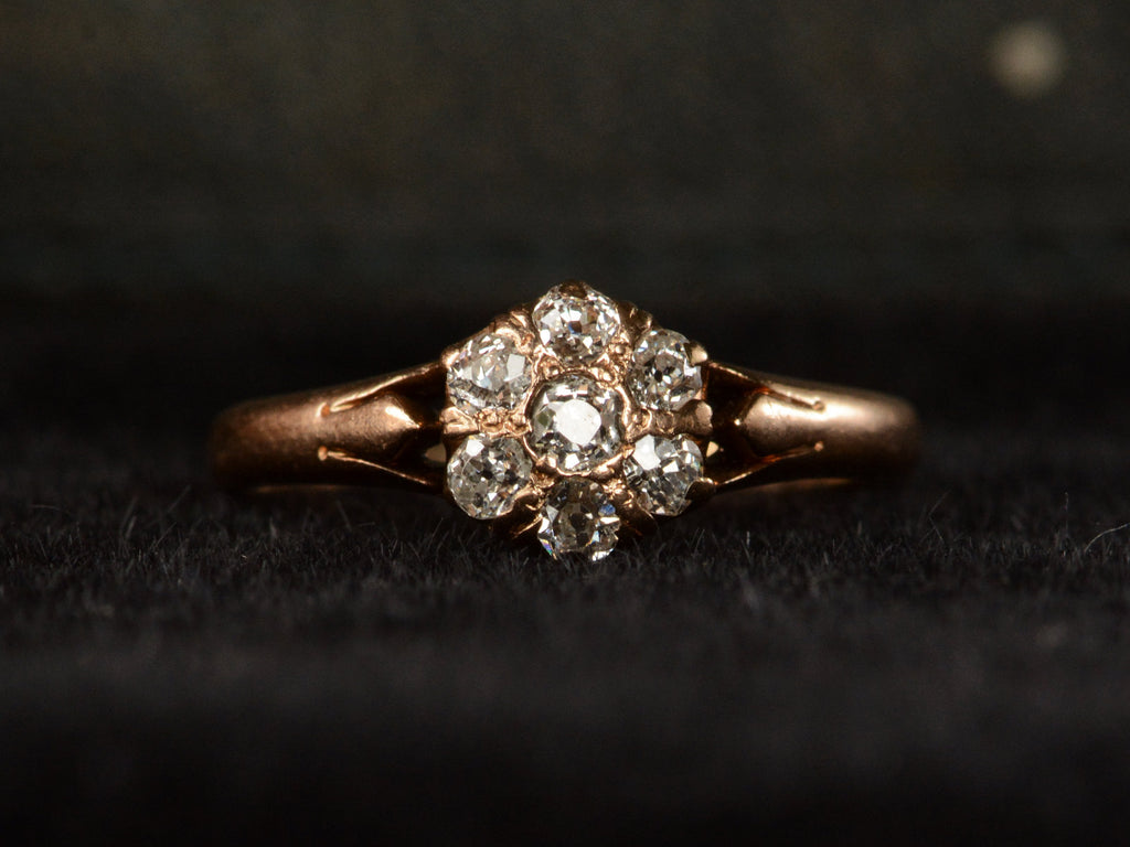 An antique rose gold Victorian ring with seven old European cut diamonds set in a cluster. Shown on dark background.