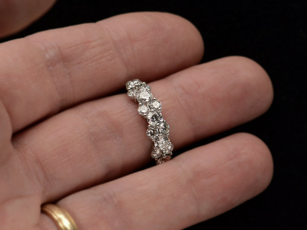 Band like platinum ring, half encrusted with a cluster of round diamonds, shown on finger.