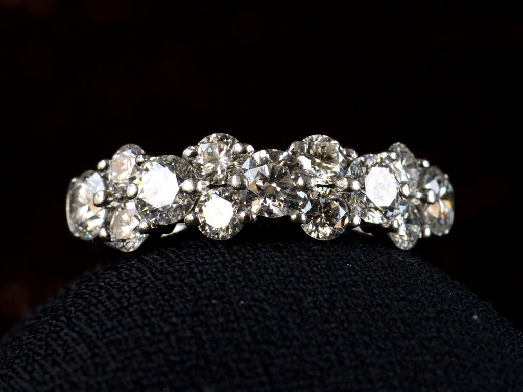 Front view of band like platinum ring, half encrusted with a cluster of round diamonds, shown on dark background. 