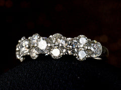 thumbnail of Right angled view of band like platinum ring, half encrusted with a cluster of round diamonds, shown on dark background. 