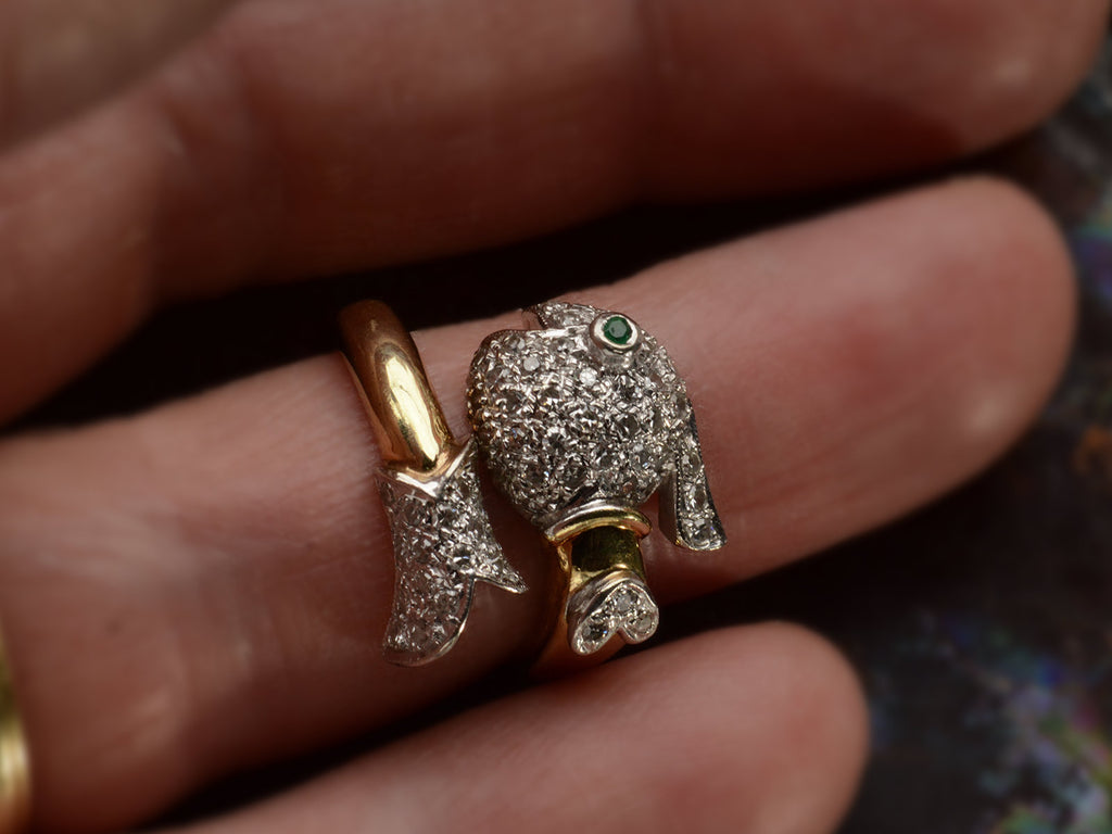 Face on view of emerald-eyed diamond studded fish ring in platinum and yellow gold, shown on finger.