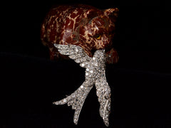 thumbnail of Vintage c1950 diamond-studded bird-shaped brooch shown balanced against carved red stone cat.