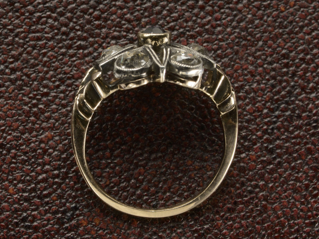 Side profile of an antique silver-topped rose gold Victorian ring with a star design centering on a blue sapphire and old mine cut diamonds set in between each point. Shown on dark textured background.