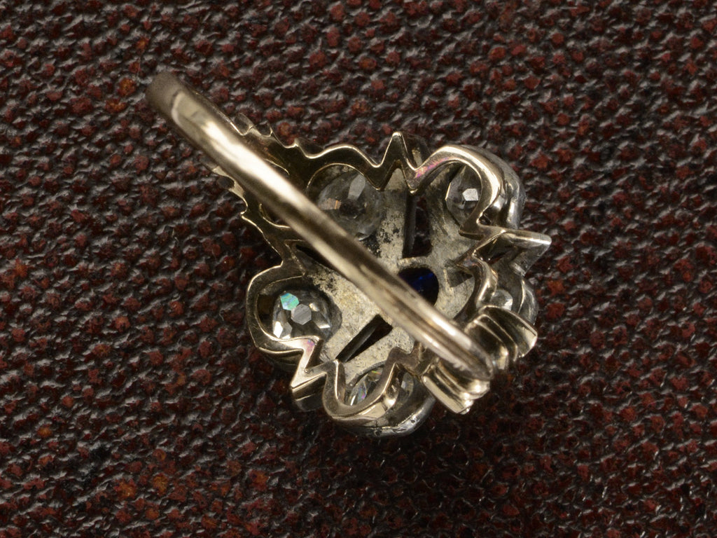 Inside view of an antique silver-topped rose gold Victorian ring with a star design centering on a blue sapphire and old mine cut diamonds set in between each point. Shown on dark textured background.