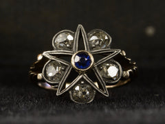 thumbnail of Front view of an antique silver-topped rose gold Victorian ring with a star design centering on a blue sapphire and old mine cut diamonds set in between each point. Shown on dark background.