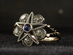 thumbnail of Angled view of an antique silver-topped rose gold Victorian ring with a star design centering on a blue sapphire and old mine cut diamonds set in between each point. Shown on dark background.