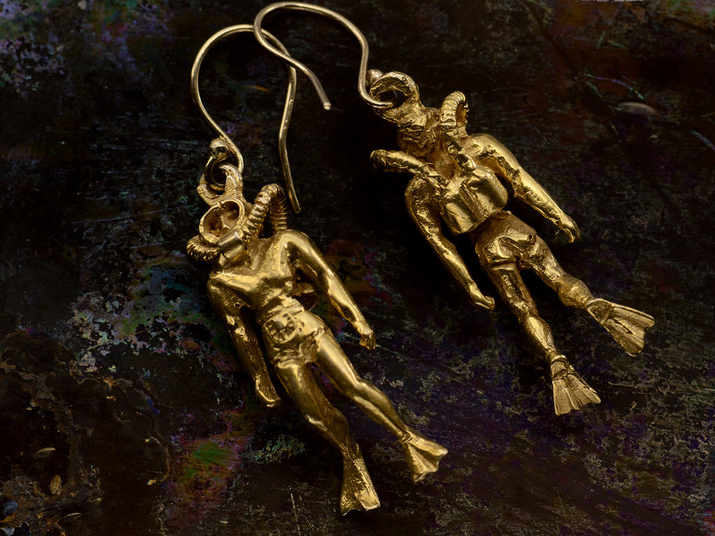 Pair of gold scuba diver earrings, one showing the backside, on dark iridescent background.