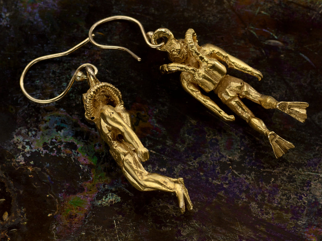Pair of gold scuba diver earrings (one showing side view and one showing backside) on dark iridescent background.