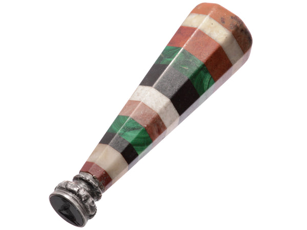 Angled view of antique wax seal with the image of a dog cut into black glass and a handle of layered red jasper, white agate, onyx and green malachite. Shown on white background.