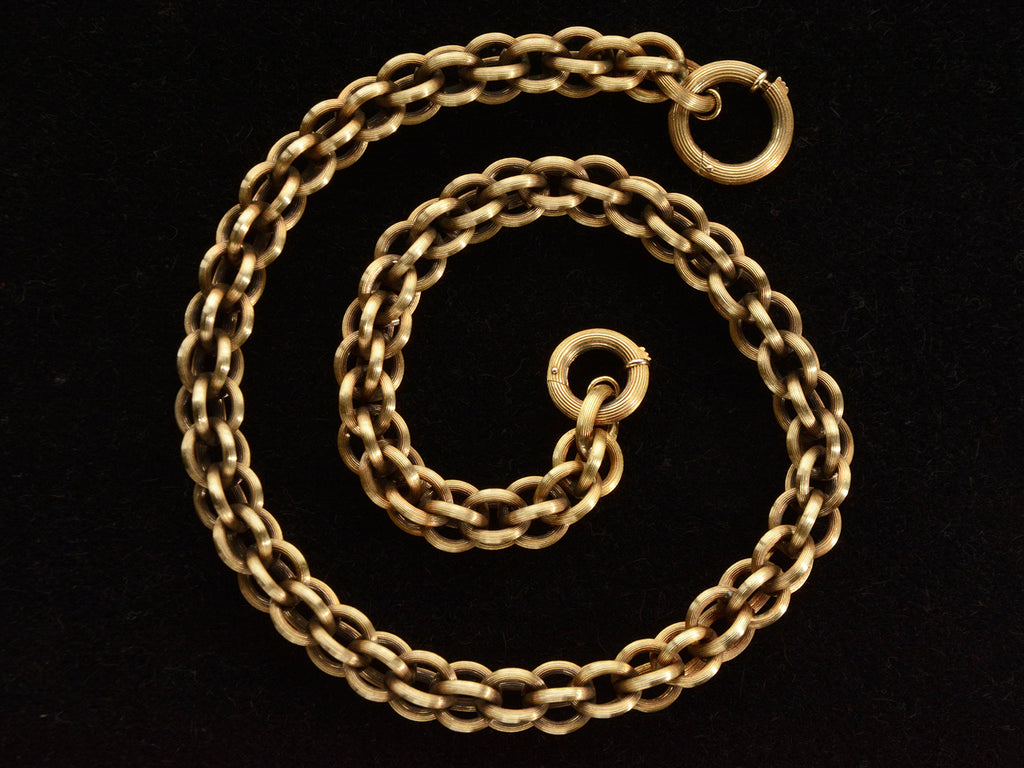 Detail view of a double-link chain necklace with reeded texture, shown spiraled on dark background.