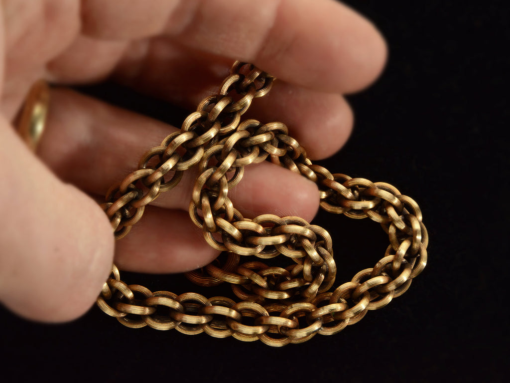 Detail view of a double-link chain necklace with reeded texture, held in hand.