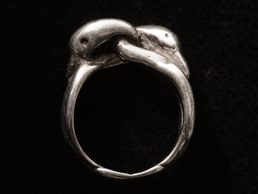 Side profile of sterling silver double swan head ring, on black background.