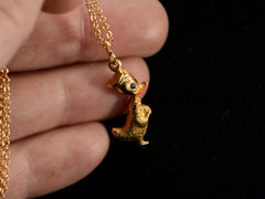 thumbnail of Detail of gold Donald Duck pendant with orange and blue enamel details, held in fingers.