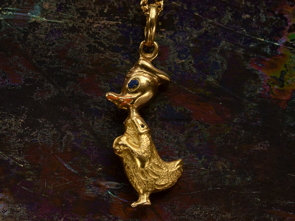 Reverse side of gold Donald Duck pendant with orange and blue enamel details shown on dark background.