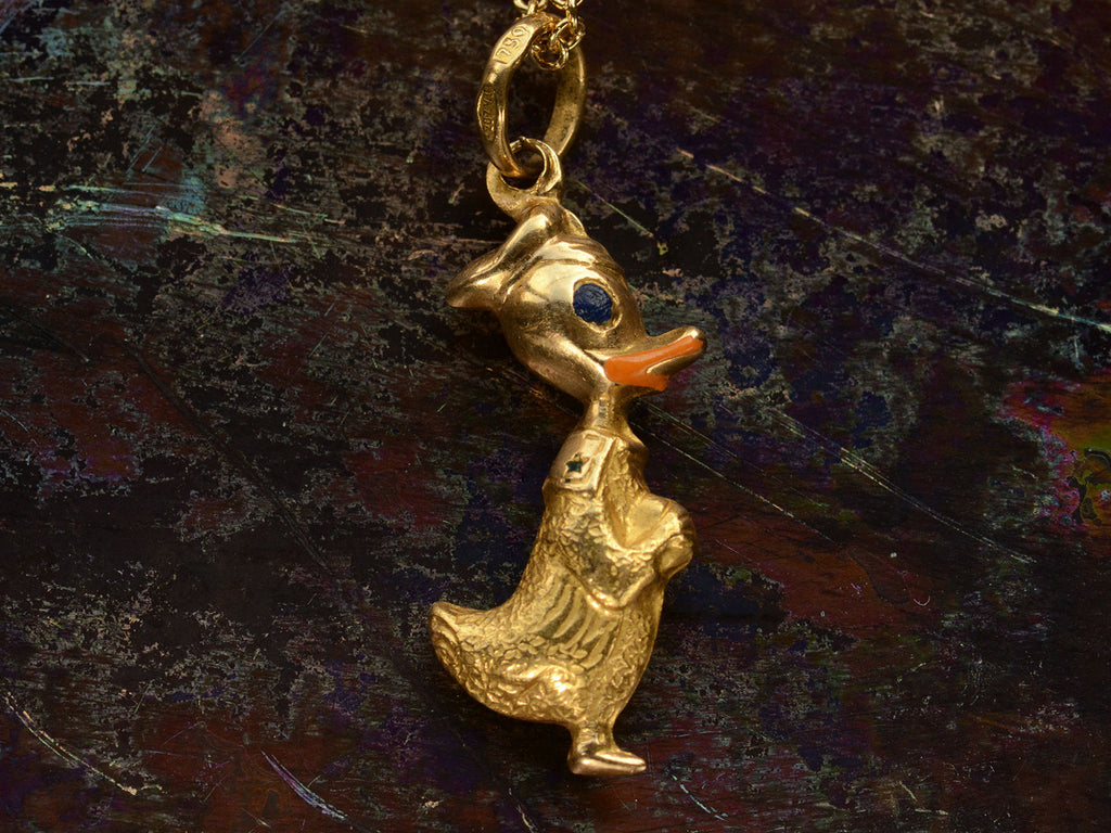 Front side of gold Donald Duck pendant with orange and blue enamel details shown on dark background.