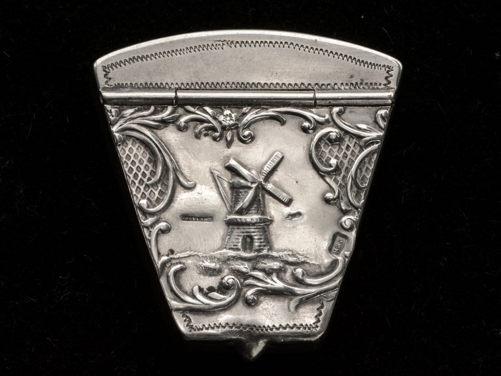 An antique silver wedge-shaped c1920 Dutch pillbox with the image of a windmill, shown on black background. A "HOLLAND" stamp is visible. 
