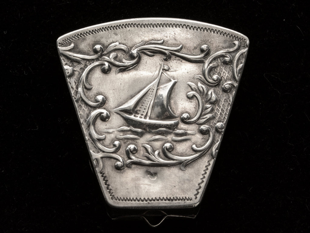 An antique silver wedge-shaped c1920 Dutch pillbox with the image of a sailboat, shown on black background.