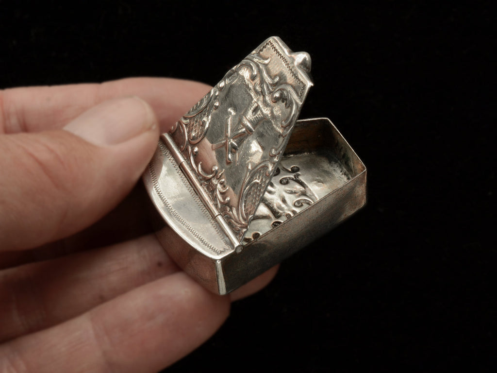 An antique silver wedge-shaped c1920 Dutch pillbox with the image of a windmill, shown open and held in hand.