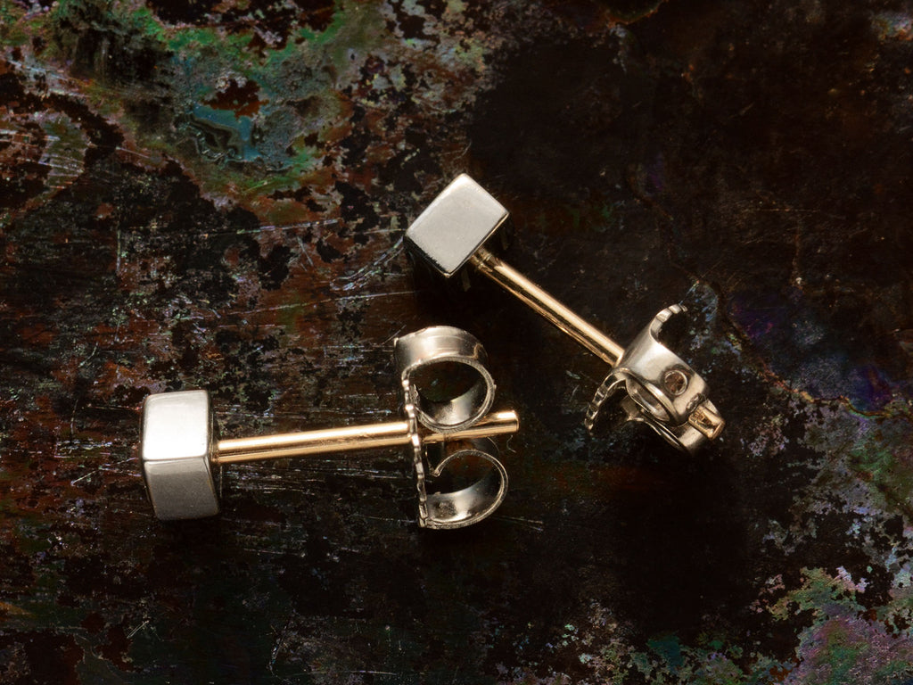 Sides of a pair of 0.19cttw square step cut white diamond stud earrings in platinum bezels with yellow gold posts, shown on dark textured background.