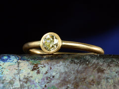 thumbnail of Right angled front view of simple EB Modern ring with a round light yellow diamond in a yellow gold bezel. Shown dark colorful background.