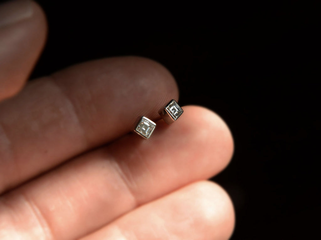 Front view of 0.35cttw Square Step Cut White Diamonds in Platinum Bezels with Yellow Gold Posts, Shown on hand for scale.