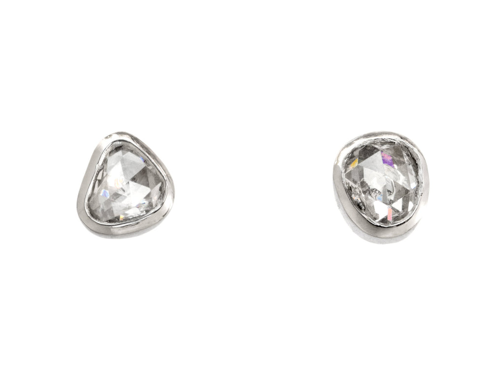 A pair of mismatched and irregular shaped rose cut diamonds set in platinum bezels as stud earrings, shown on white background