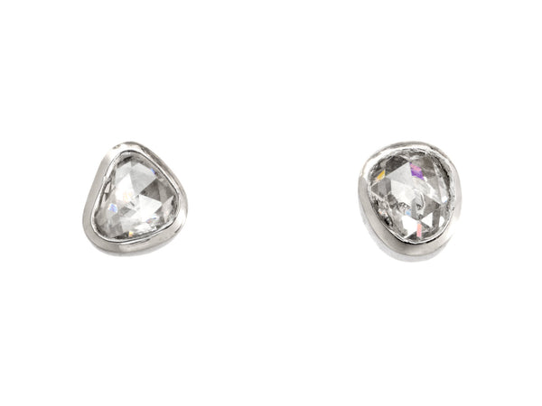 A pair of mismatched and irregular shaped rose cut diamonds set in platinum bezels as stud earrings, shown on white background