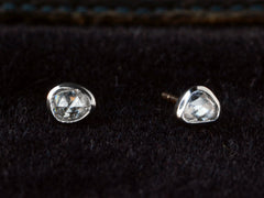thumbnail of A pair of mismatched and irregular shaped rose cut diamonds set in platinum bezels as stud earrings, shown on dark background