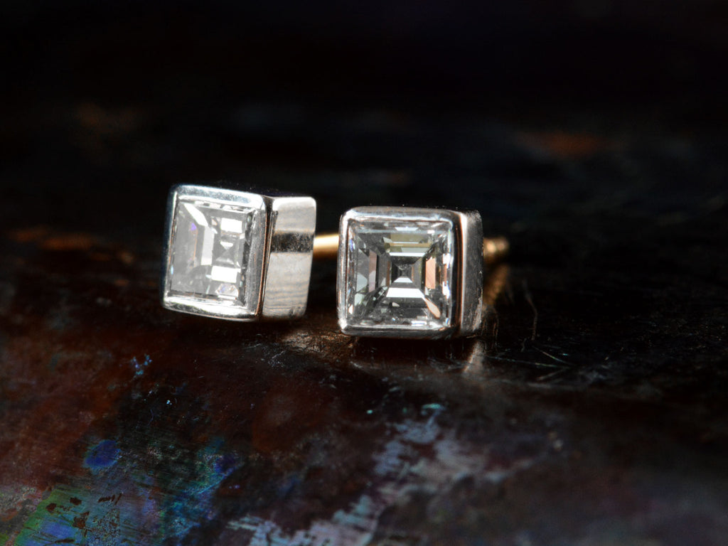 Front angled view of a pair of 0.52cttw Square Step Cut Diamonds Studs in Platinum Bezels with Yellow Gold Posts (on dark textured background)