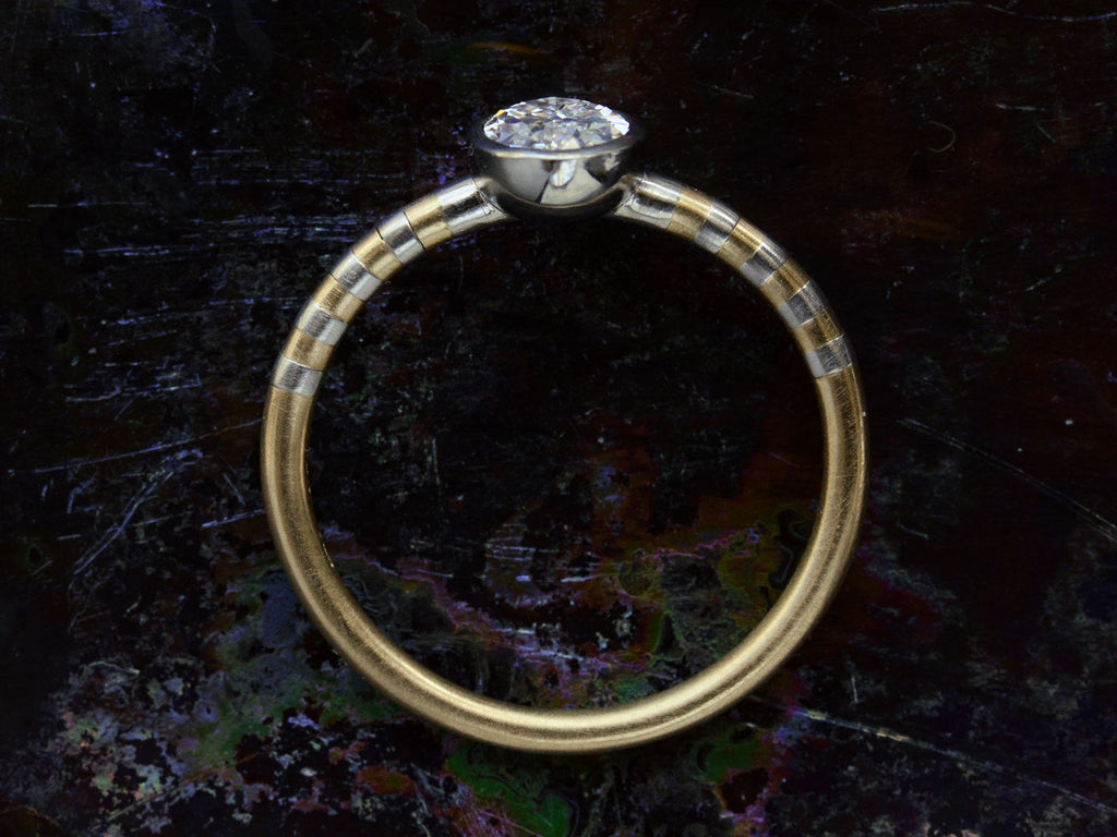 Side profile view of EB 0.69ct Oval Diamond Ring with Platinum Bezel and Striped Gold and Platinum Band (shown on dark background)