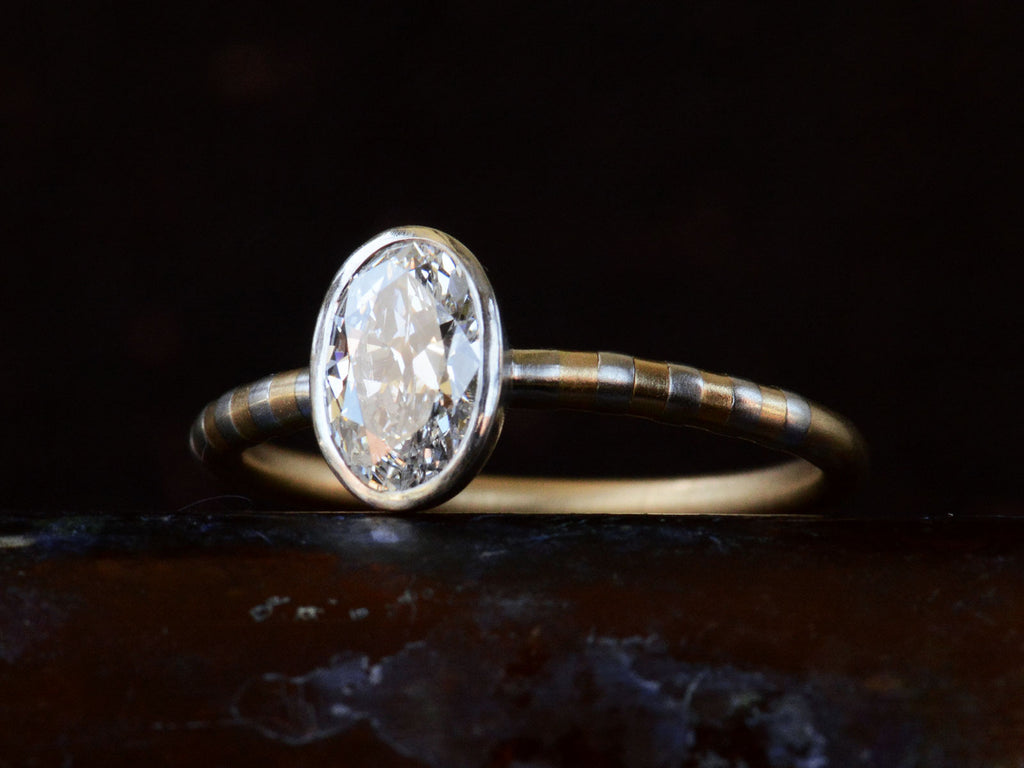 Angled view of EB 0.69ct Oval Diamond Ring with Platinum Bezel and Striped Gold and Platinum Band (shown on dark background)
