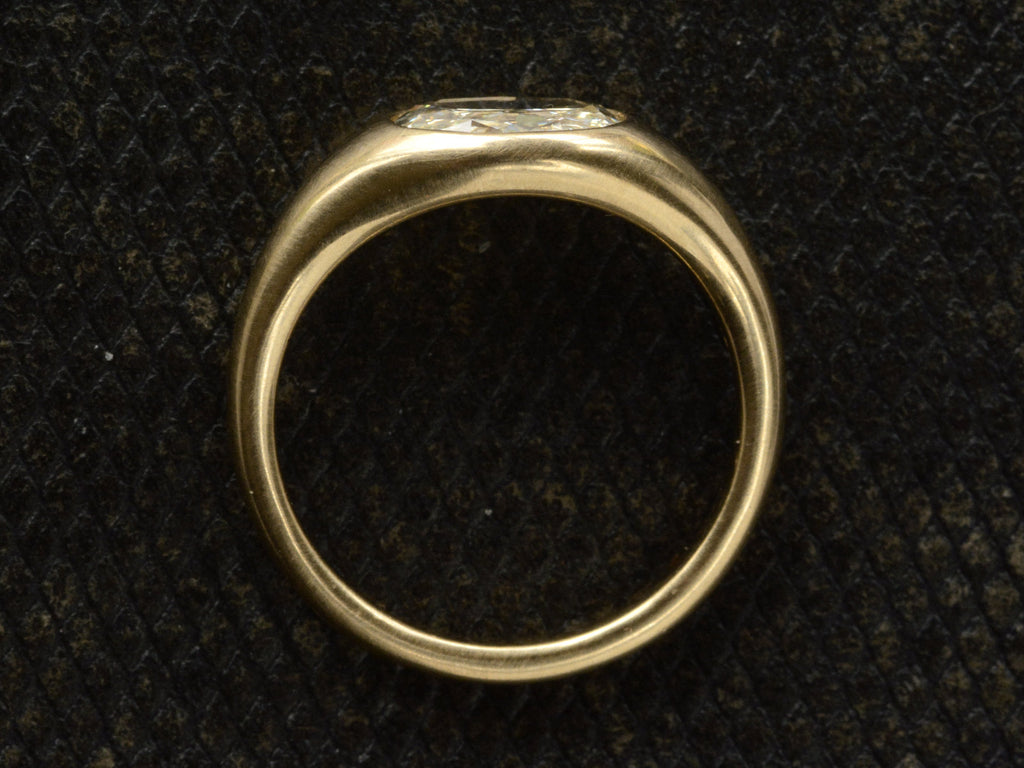 Side profile of flush set oval diamond ring in yellow gold, shown on dark background.