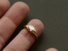 thumbnail of Flush set oval diamond ring in yellow gold, shown on finger against dark green background.