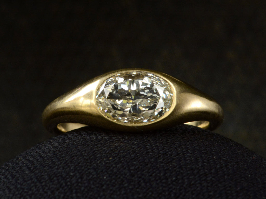 Flush set oval diamond ring in yellow gold, shown on dark background.
