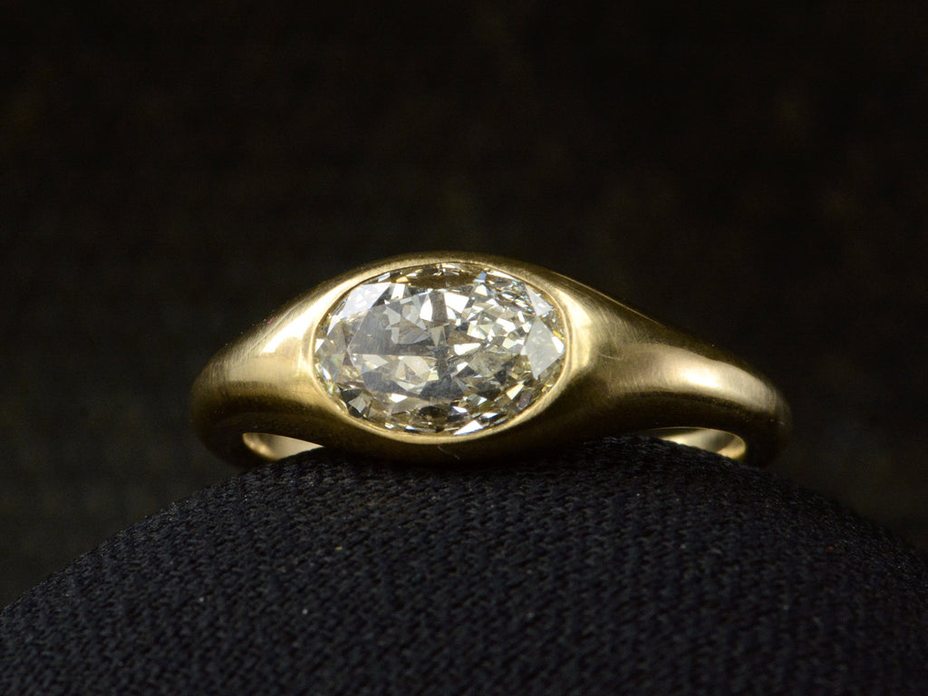Right front angled view of flush set oval diamond ring in yellow gold, shown on dark background.