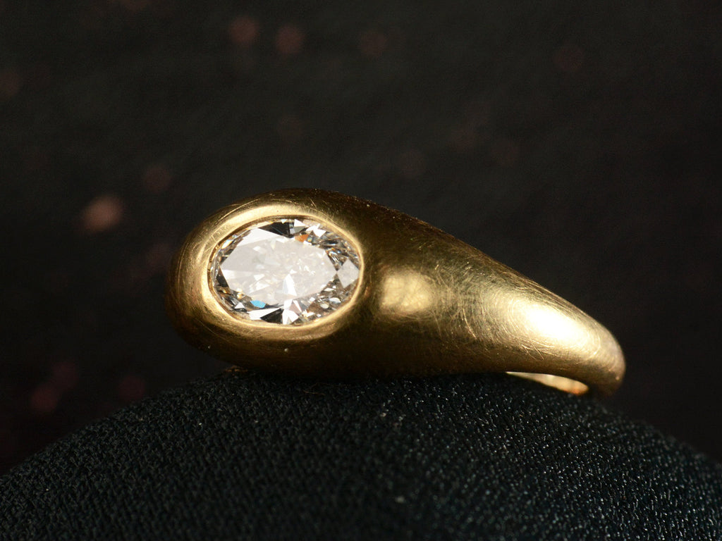Right angled front view of EB Modern flush set oval white diamond in rounded 22K yellow gold setting, shown on dark background.
