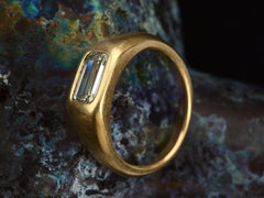 thumbnail of Angled side view of EB Modern engagement ring with elongated emerald cut diamond flush set in a rounded 22k yellow gold mounting, on dark background.