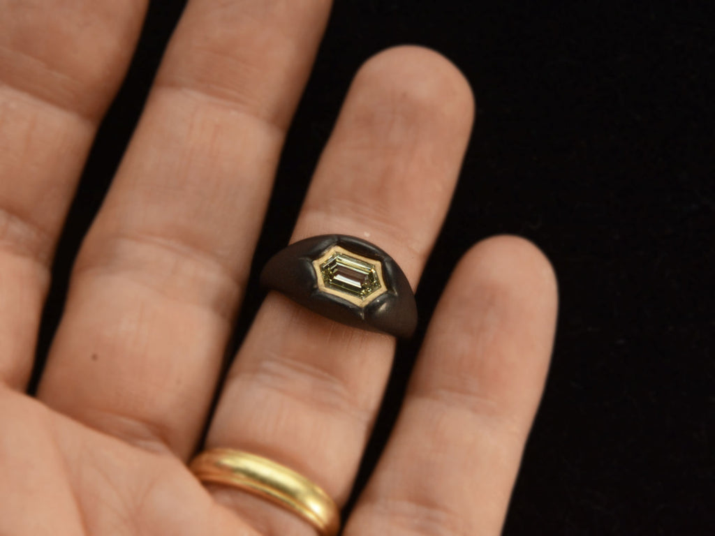 Front view of EB Modern hexagonal light yellow diamond set in yellow gold bezel sunken into pillowy blackened silver mounting (shown on hand)