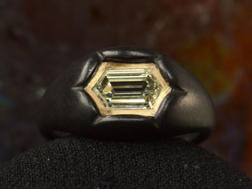 Front view of EB Modern hexagonal light yellow diamond set in yellow gold bezel sunken into pillowy blackened silver mounting (shown on dark background)