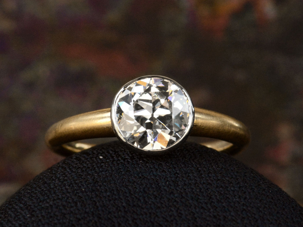 Diamond detail of EB Modern engagement ring with 1.42ct round diamond set in platinum bezel with round 18K yellow gold shank. Shown on dark background.