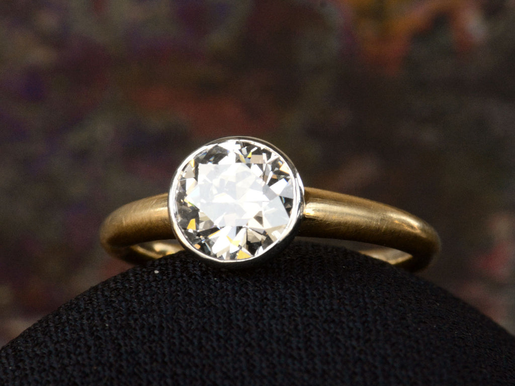 Angled view of EB Modern engagement ring with 1.42ct round diamond set in platinum bezel with round 18K yellow gold shank. Shown on dark background. 