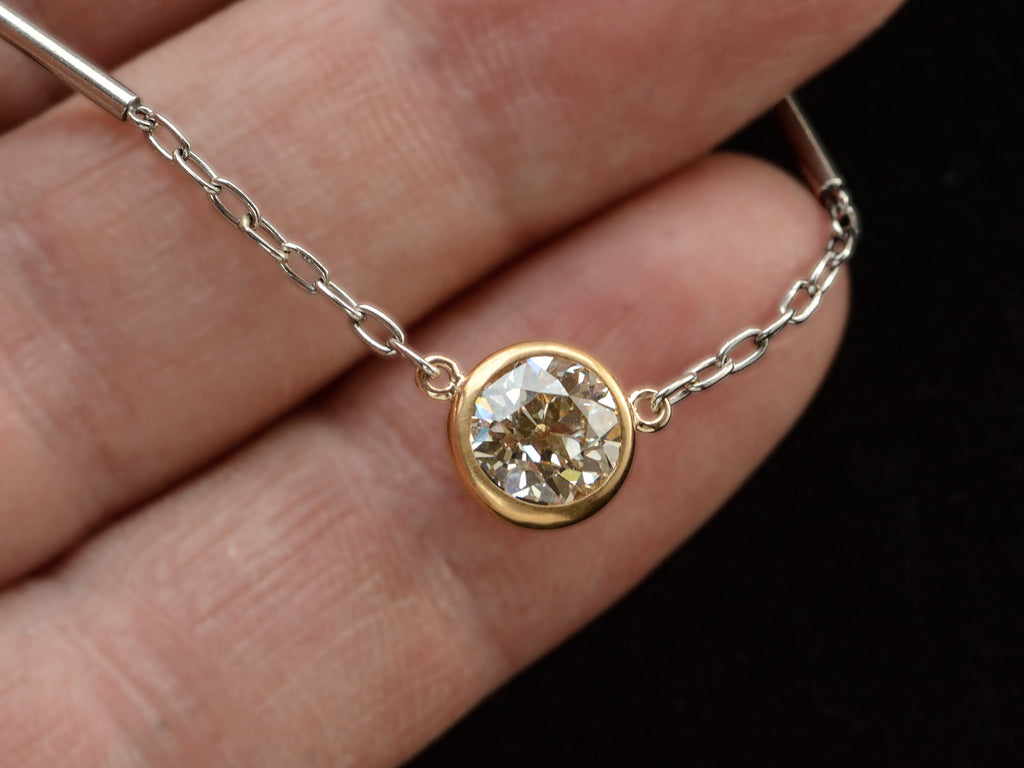 Detail of EB Modern necklace with round old cut diamond set in 22K yellow gold bezel on platinum chain. Shown held in hand.