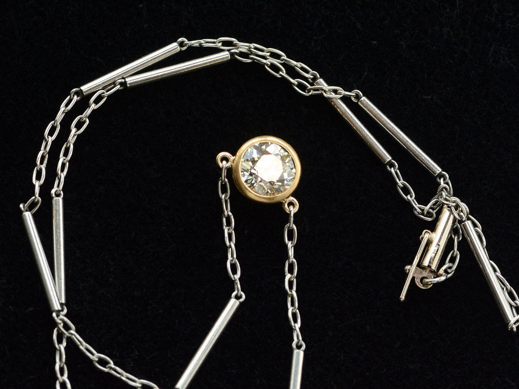 Detail of EB Modern necklace with old cut round diamond shown in 22k yellow gold bezel  on platinum chain. Shows 14K white gold clasp. Shown on black background.